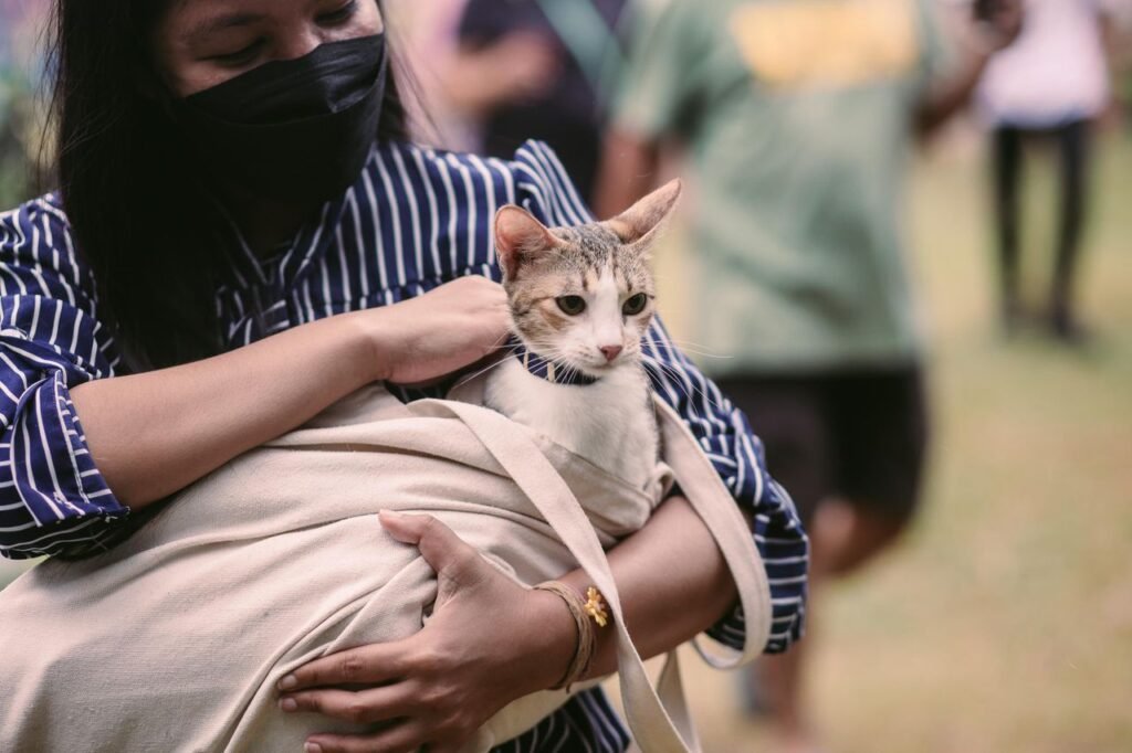 A woman holding a cat wrapped in fabric during a daytime outdoor event.